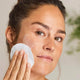 Woman applying facial cleanser and toner with a cotton pad.